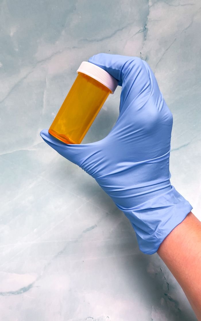 Close-up of a gloved hand holding an empty pill bottle against a marble backdrop, emphasizing healthcare themes.