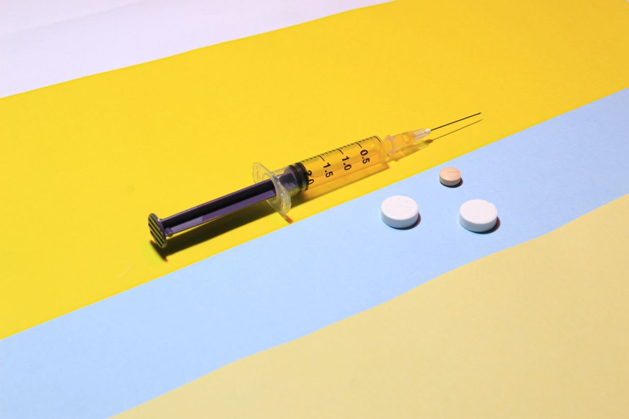 services-01 A syringe and pills on a vibrant yellow and blue background, depicting healthcare theme.