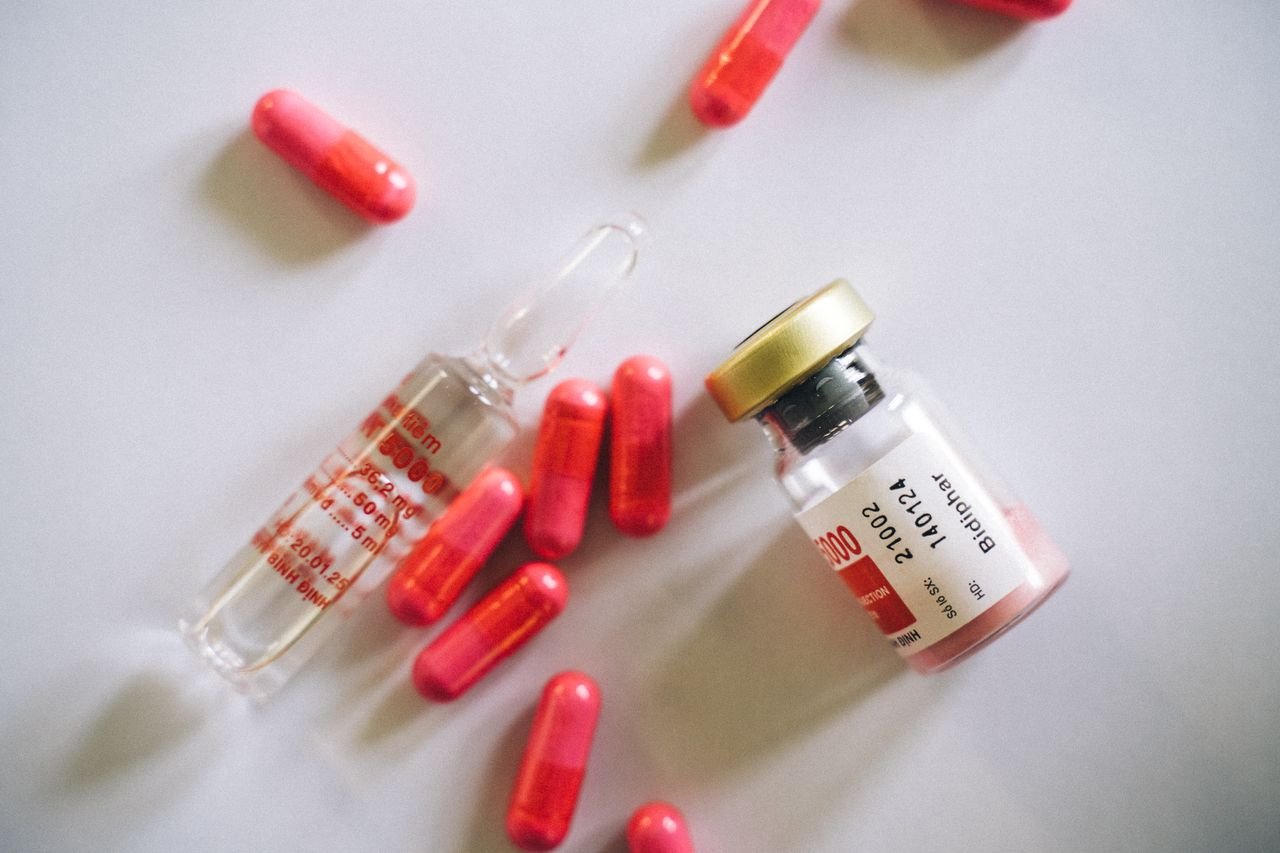 services-02 Flat lay of medication bottle, glass vial, and red capsules on a white surface.